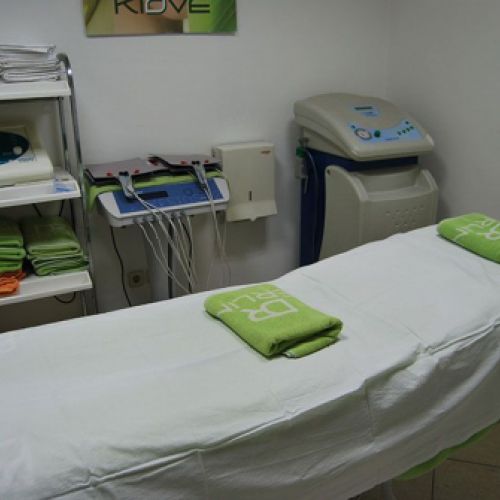 Sala con camilla con toallas verdes y aparatología electrónica para tratamientos de belleza